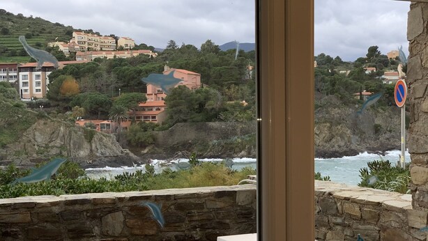 A coastal view from a balcony with a stone wall, a tiled table, and a butterfly decoration. - Apartment less than 30m from the sea Fiber Internet (Collioure)