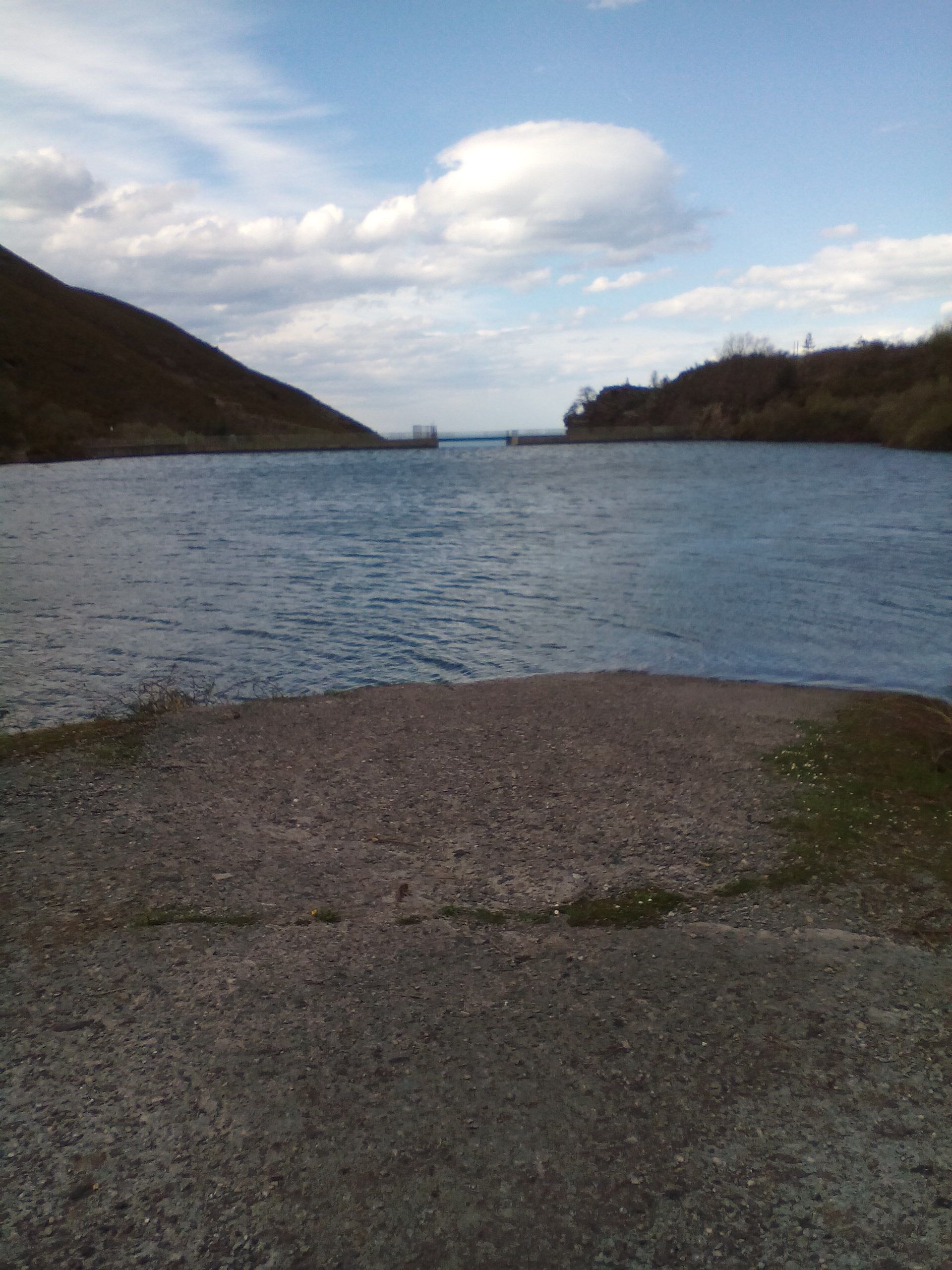 A river with a bridge in the distance, surrounded by hills.