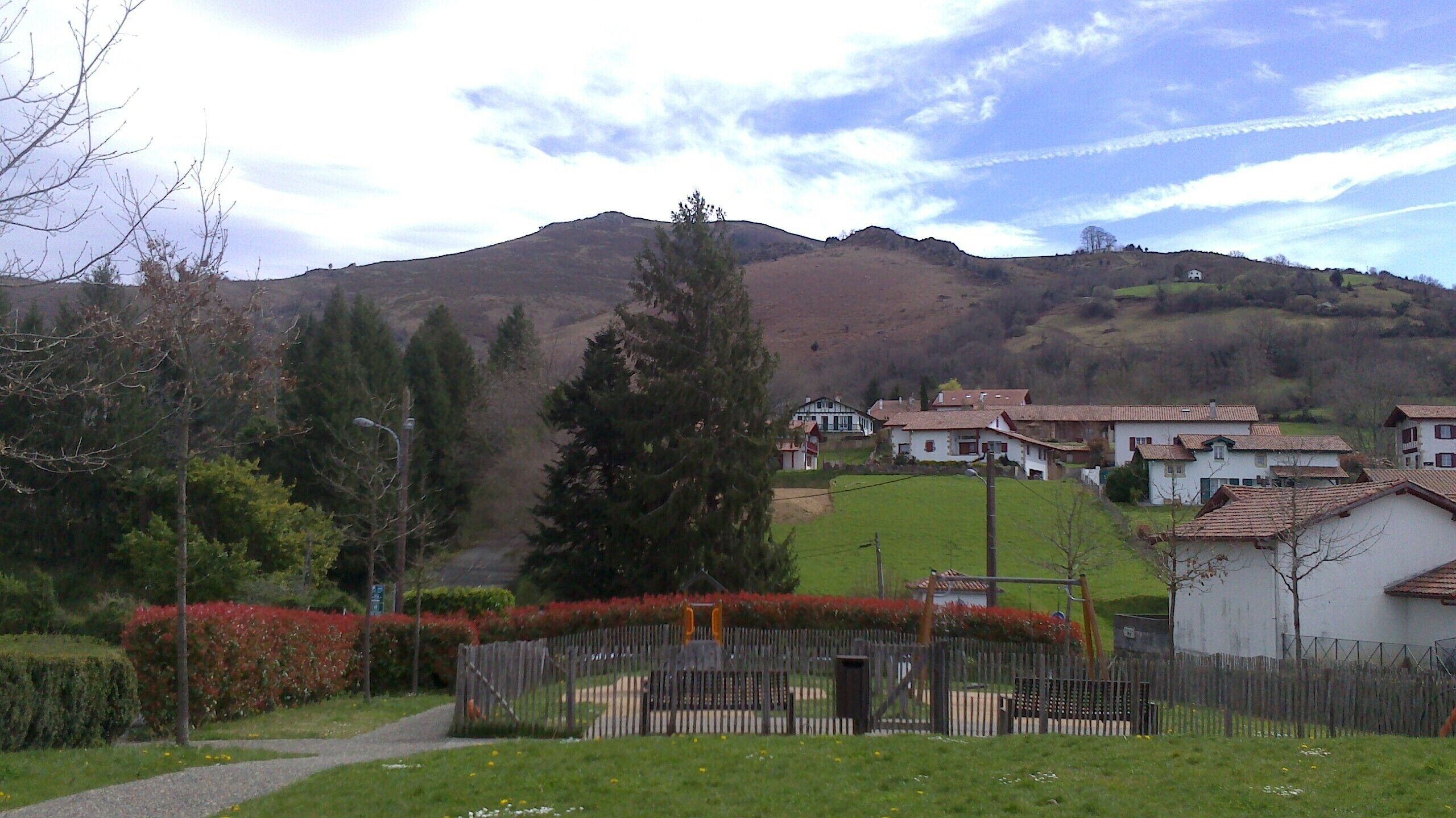 A rural village with traditional houses, a grassy area, and a hill in the background.