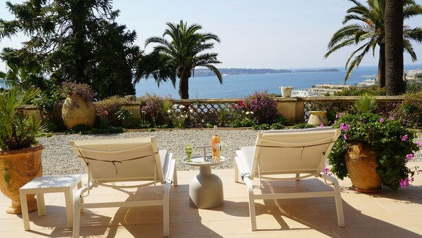 A terrace with two white chairs and a small table, overlooking a scenic view of the sea and palm trees. - Fantastic 180° sea view, charm of bygone days, space and confort (Cannes)