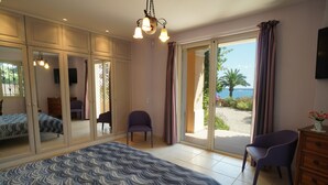 A bedroom with a large bed, a desk, and a chair. There is a sliding glass door leading to an outdoor area with a view of the sea. - Fantastic 180° sea view, charm of bygone days, space and confort (Cannes)
