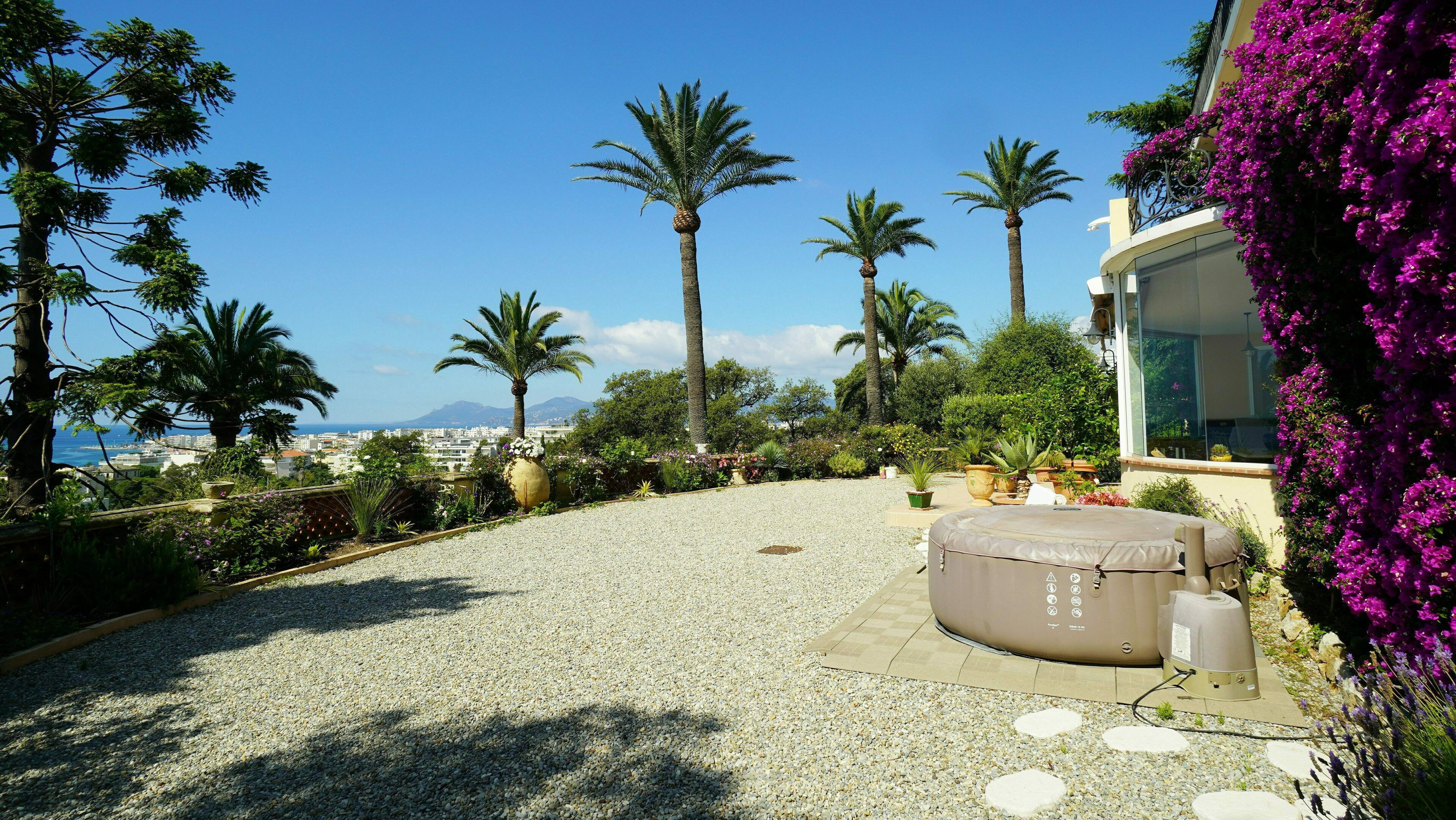 A patio area with a hot tub, surrounded by gravel, palm trees, and a view of the city and mountains.