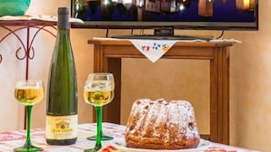 A room with a television displaying a nighttime cityscape, a table with a bottle of wine, glasses, and a dessert. - Terraced country house, 10 minutes from the slopes, at the foot of the mountains  (Breitenbach-Haut-Rhin)