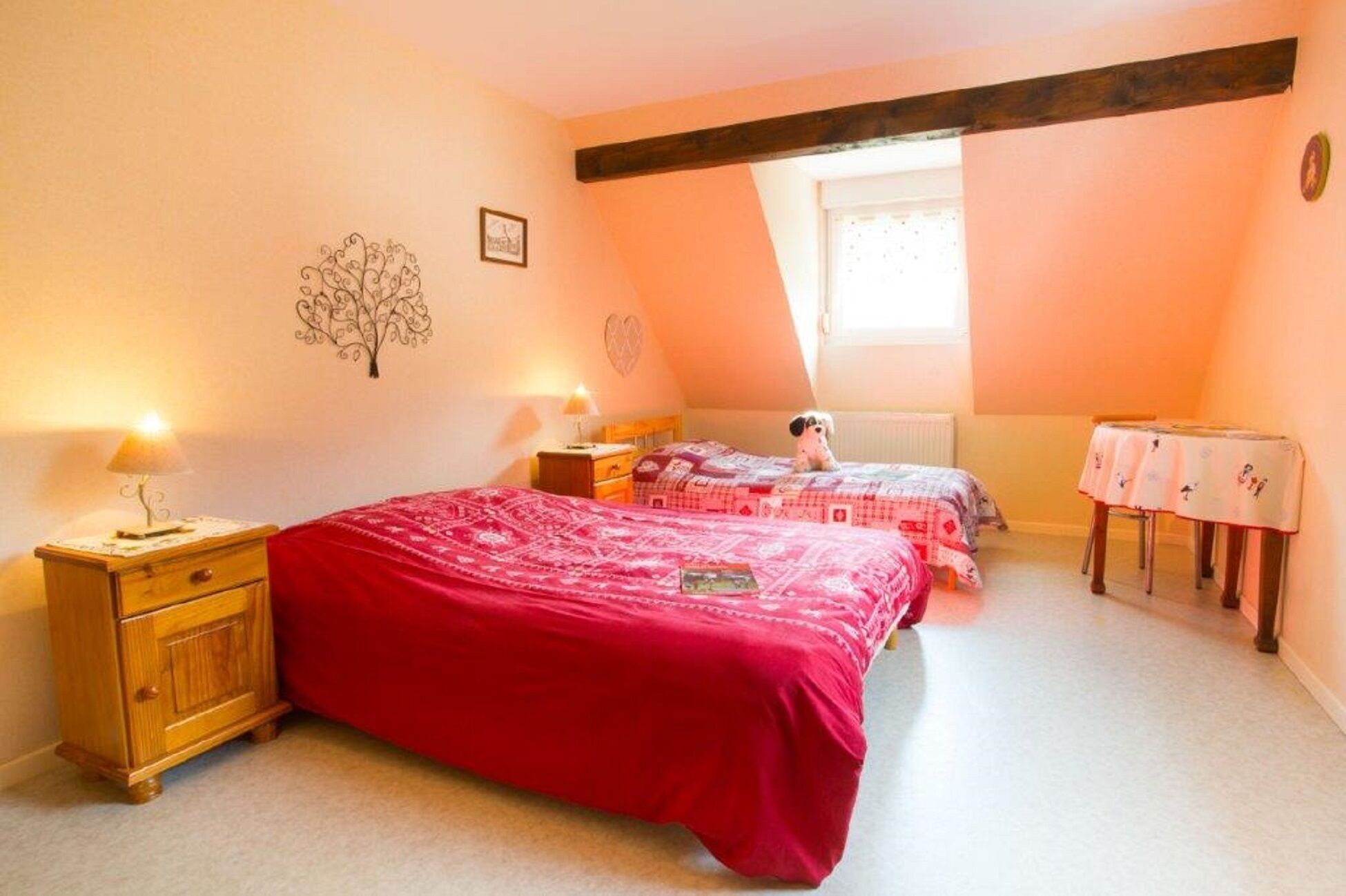 Une chambre avec deux lits, une commode en bois, une petite table et une fenêtre.
