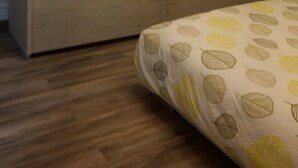 A bedroom with a wooden wardrobe, a bed with a leaf-patterned duvet, and a ceiling light fixture. - APARTMENT 1ST FLOOR 4 ROOMS 2 BEDROOMS 2-4PERS (Colmar)