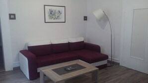 A living room with a red sofa, a small wooden coffee table, a floor lamp, and a framed artwork on the wall. - APARTMENT 1ST FLOOR 4 ROOMS 2 BEDROOMS 2-4PERS (Colmar)