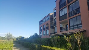 A multi-story building with balconies, a clear sky, and a pathway lined with greenery. - Studio cabin 4 pers, in quiet residence with swimming pool, 50 m from the beach (Saint-Cyprien)