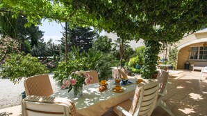 An outdoor dining area with a table set for two, surrounded by wicker chairs, under a tree canopy. - Apartment in traditional farmhouse with swimming pool for 2 people, 2 bedrooms (Saint-Rémy-De-Provence)