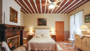 A bedroom with a wooden ceiling, a fireplace, a bed with white bedding, two bedside tables with lamps, and a wooden door. - Apartment in traditional farmhouse with swimming pool for 2 people, 2 bedrooms (Saint-Rémy-De-Provence)