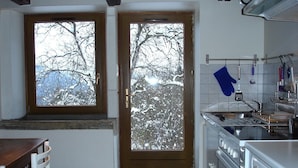 A kitchen with a stove, oven, and sink. There is a window with a view of snow-covered trees. - Old Farmhouse (Rupt-Sur-Moselle)