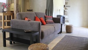 A living room with a grey sofa, black coffee table, wicker ottoman, and a woven rug. - Charming cottage in peace between countryside and sea! With family, friends ......... (Sougéal)