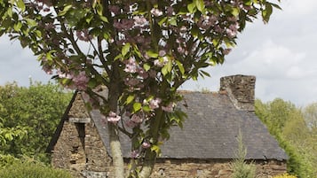 Une maison en pierre avec un toit de chaume, entourée d’un jardin où poussent différentes sortes de fleurs et d’arbustes.
