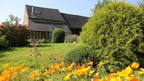 A house with a sloped roof, surrounded by a well-maintained garden with various plants and a field of yellow flowers. - Charming cottage in peace between countryside and sea! With family, friends ......... (Sougéal)