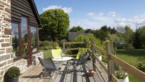 A wooden deck with outdoor furniture, a stone wall, and a large tree in the background. - Charming cottage in peace between countryside and sea! With family, friends ......... (Sougéal)