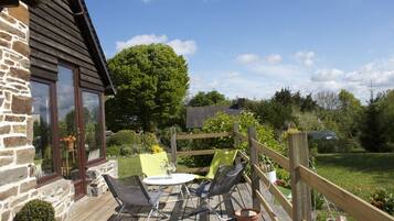 Une terrasse en bois avec des meubles d’extérieur, un mur en pierre et un grand arbre en arrière-plan.