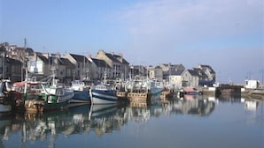 Ein Hafen mit vertäuten Booten, Gebäuden an der Uferpromenade und einem klaren Himmel.