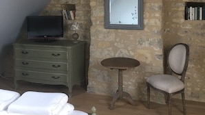 Ein Schlafzimmer mit schrägen Wänden, Steinwänden, einem Bett, einem Schminktisch, einem Fernseher, einem kleinen Tisch und einem Stuhl.