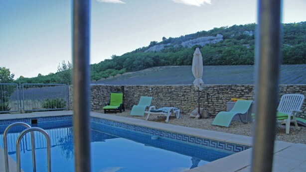 A swimming pool with lounge chairs and an umbrella, surrounded by a stone wall and greenery. - Large traditional stone house with swimming pool (Murs)