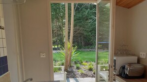A kitchen with a sink, a toaster, and a view of a garden through an open door. - Warm house in the heart of a forest, close to shopping and beaches (Fouesnant)