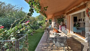 Patio esterno con tavolo e sedie, immerso nel verde e circondato da un muro in pietra.