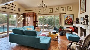 Un soggiorno spazioso con un divano grande, una poltrona e un camino. Diverse immagini incorniciate adornano la parete e un lampadario pende dal soffitto.