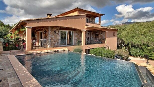 Una casa a due piani con piscina, facciata in pietra e un balcone con vista sulla piscina.