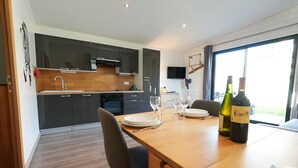 A modern kitchen with dark cabinets, a wooden countertop, and a dining area with a table set for two. - Cottage by the sea and close to the town center in Cabourg. (Cabourg)