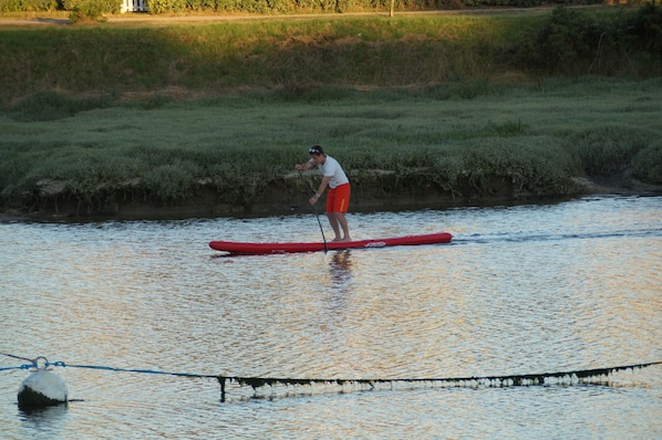 A person standing on a red paddleboard in a body of water.