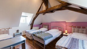 A cozy attic bedroom with two beds, a table, and a window.