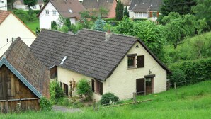 Una casa tradizionale con tetto spiovente, un piccolo giardino e una recinzione in legno.