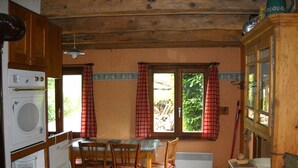 Una cucina con mobili in legno, un tavolo con sedie, una finestra con tende e un termosifone.