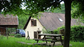 Una casa in legno rustica con tetto spiovente, un piccolo annesso e un tavolo da picnic di fronte.