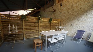 Un patio al aire libre con una mesa y sillas de madera, un taburete pequeño y una silla plegable.