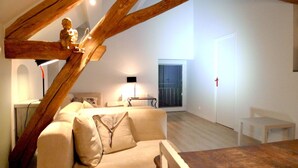 Una sala de estar moderna con techo alto, vigas de madera a la vista, un sofá blanco, una mesita y una ventana con persianas.