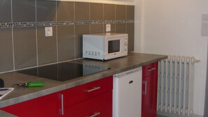 Una cocina compacta con armarios rojos, un microondas blanco y un refrigerador pequeño.