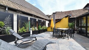 An outdoor patio area with lounge chairs, a dining table, and chairs. There are black decorative panels with plant motifs on the walls. - Manala ***, Alsatian house for 7 to 9 people in Kaysersberg - 3 bedrooms, 2 bathrooms, veranda (Kaysersberg-Vignoble)
