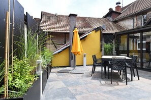A patio area with a table and chairs, a yellow wall, and a tiled floor. - Manala ***, Alsatian house for 7 to 9 people in Kaysersberg - 3 bedrooms, 2 bathrooms, veranda (Kaysersberg-Vignoble)