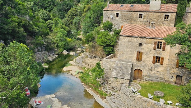 A stone building with a tiled roof, a small courtyard, and a river.