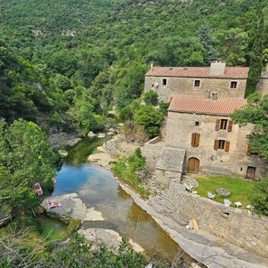 Ein Steinhaus mit Ziegeldach, einem kleinen Innenhof und einem Fluss.