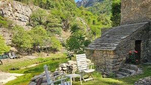 A rustic stone building with a small porch, a pond, and outdoor seating.