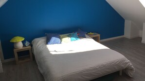 Une chambre avec un plafond en pente, un lit avec un matelas blanc et plusieurs oreillers, une table de chevet avec une lampe, et une petite table avec un bol.