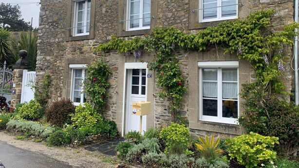 Un bâtiment en pierre doté de nombreuses fenêtres, d’une porte et d’une boîte aux lettres.