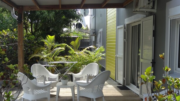 Une terrasse couverte avec une plateforme en bois, des meubles en osier blanc et des plantes en pot.