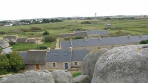A stone building with a flat roof, surrounded by large rocks and green fields.