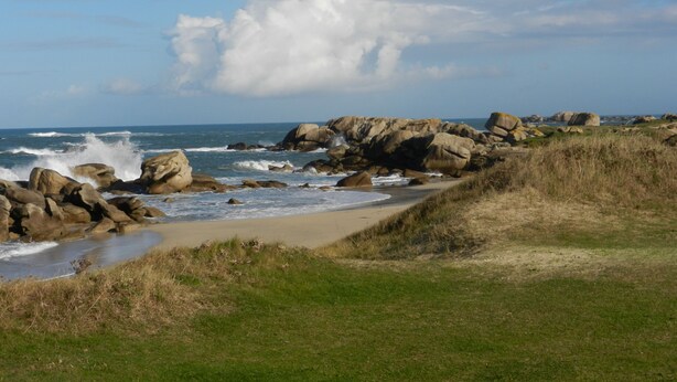 A coastal landscape with large rocks, a sandy beach, and the ocean.