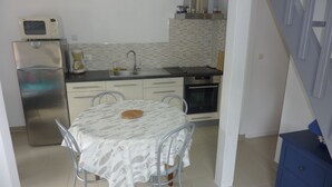 A compact kitchen with a refrigerator, microwave, sink, and oven. There is a dining table with chairs and a patterned tablecloth.