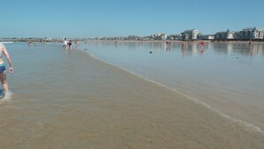 A wide beach with people walking and swimming, and buildings in the background.