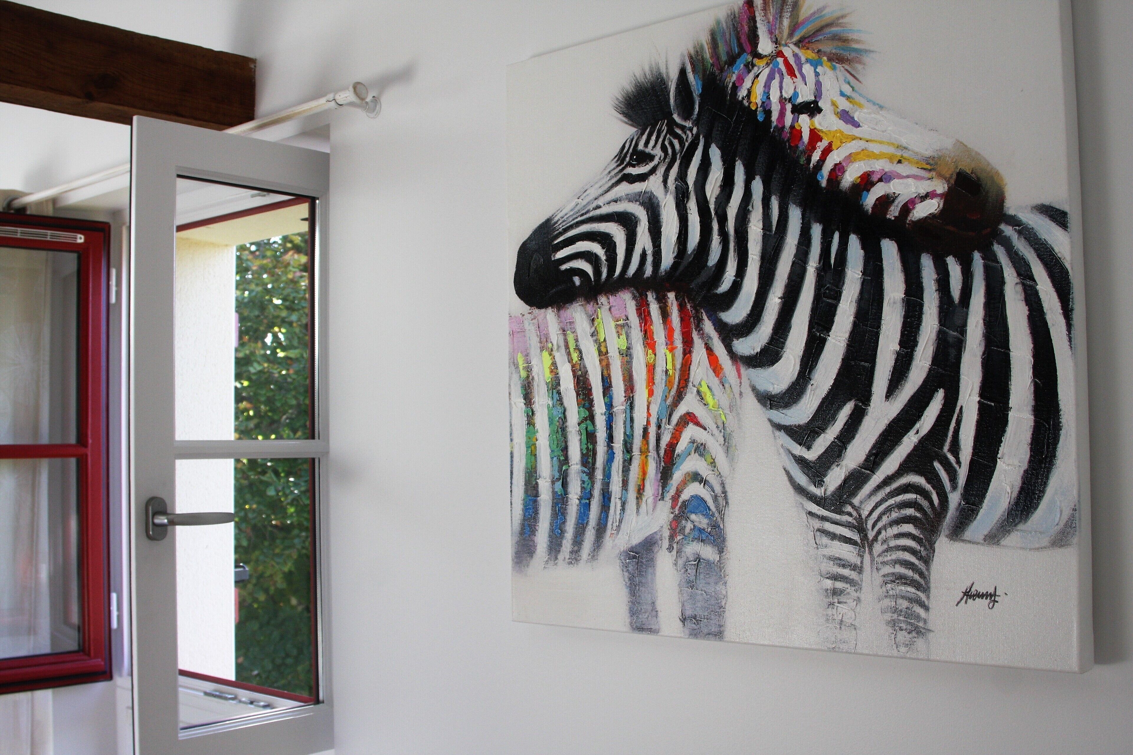 En målning av en zebra på en vägg, ett fönster med en röd ram och en träbalk ovanför fönstret.