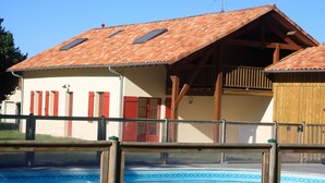 Un edificio con piscina, balcón de madera y persianas rojas.