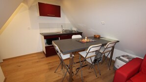 Une cuisine compacte comprenant une table et des chaises, un meuble rouge et une petite poubelle.